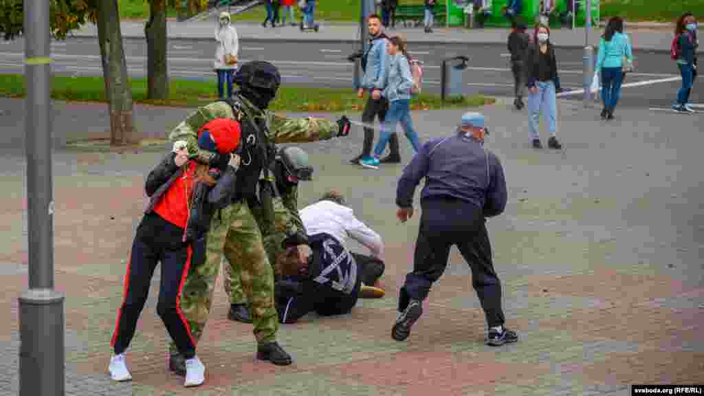 Боец в форме цвета хаки без опознавательных знаков держит девушку за шею, одновременно применяет газ в отношении другого протестующего. 27 сентября, Гродно.